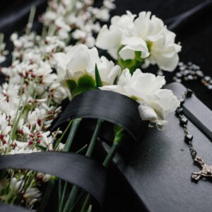 Close-up of white flowers and rosary on dark cloth, symbolizing mourning and spirituality.