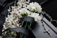 Close-up of white flowers and rosary on dark cloth, symbolizing mourning and spirituality.